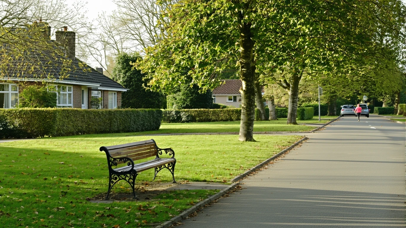 A well-maintained neighborhood park with a bench and path, seen from across a quiet suburban street lined with homes.